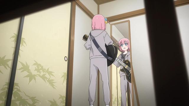 A shy pink-haired anime girl in a grey tracksuit is holding a guitar for the first time. She looks at her reflection in the mirror and sees  herself looking cool.
