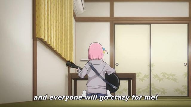 The pink haired girl is kneeling before a low table, and starting to learn to play guitar for the first time. She believes that learning the instrument will make people like her, and she can overcome her shyness