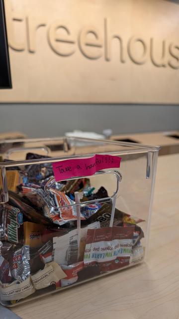 Photo of the Treehouse store checkout counter showing the wooden Treehouse sign and a clear container of fun sized candy and a note reads: take a handful!!!