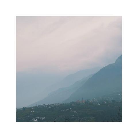 a subtle square image showing the details of a cloudy mountainscape. the sky is hazy after some rain but the early light is already coming through again. the layers of hills become more and more vague towards the distance