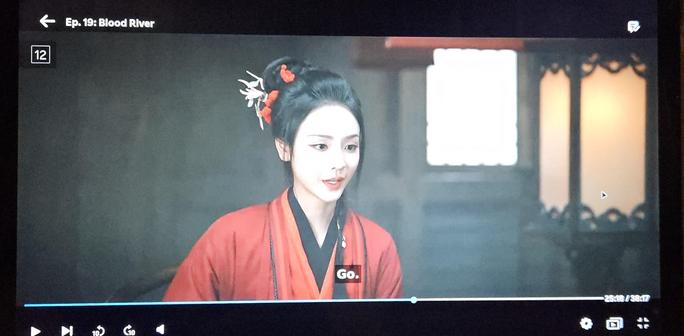 Woman in red looking down on something off-screen, saying "Go."