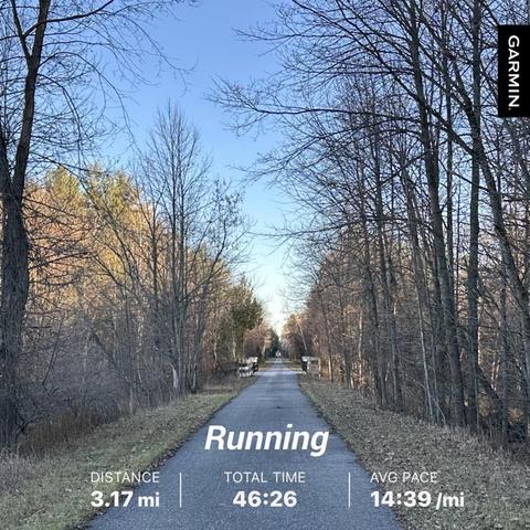 A scenic view of a running path flanked by trees and features blue sky with scattered clouds. Overlaid on the image are statistics: distance of 3.17 miles, total time of 46:26, and an average pace of 14:39 per mile.