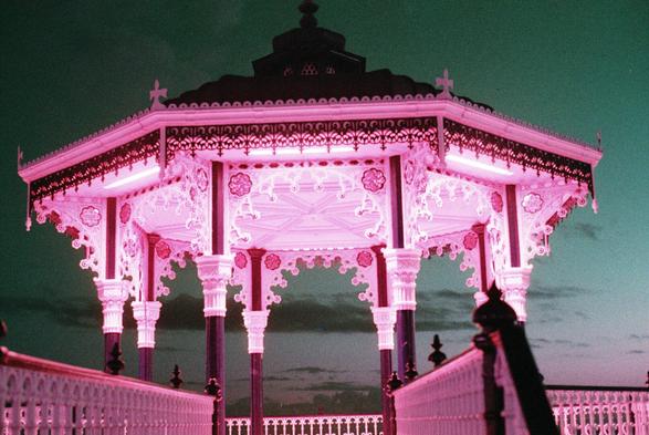 The brighton beach band stand at night, with a turquoise dusk sky, and lit up in purple due to the film stock