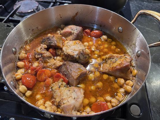 Pot with stew including meat cubes, small tomatoes and many ceci (chickpeas)