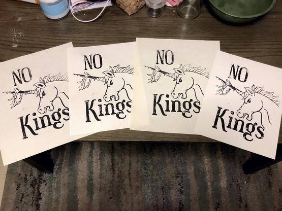 four prints laid out on a tabletop, two on larger cream colored paper and two on slightly smaller white paper. the print is the same as the blocks above, but the ink has not transferred evenly and the words are distinctly patchy