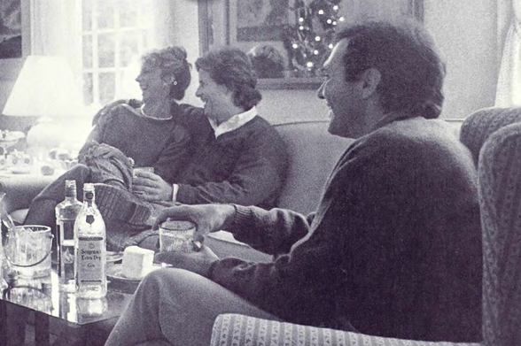 1987 Vintage Social Gathering in a Living Room

A black-and-white photograph depicting three individuals seated on a couch, engaged in conversation with beverages placed nearby.
The room is adorned with festive decorations including what appears to be a Christmas tree.