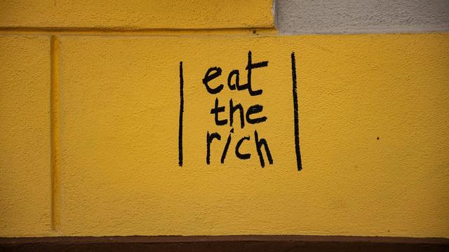 Graffiti auf einer gelb gestrichenen Mauer, geschrieben mit einem schwarzen Stift: "eat the rich"