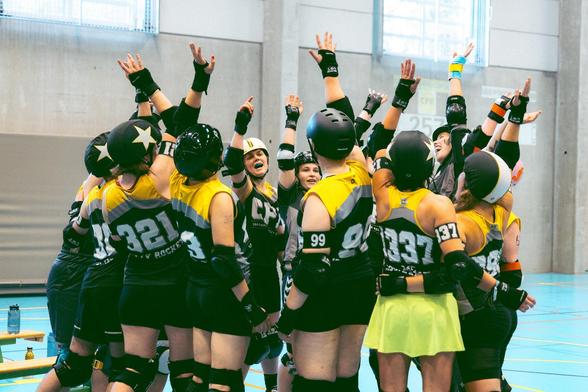 Foto og 15 people stranding in circle and raising there hands. They are wearing black and yellow sport cloth, helmets and knepads.
