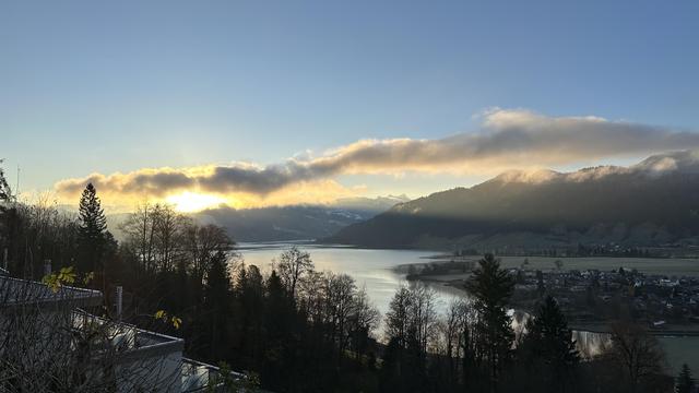 Sun just beginning to rise over hills and lake behind a single band of low-lying clouds.