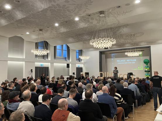 The opening plenum of a conference in a ballroom with a hundred people facing the speaker