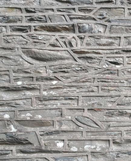 A wall made of rough grey/brown irregular stones. The mortar is proud of the stones and forms neat lines between the stones. Many of the stones are almost long rectangles; they are contrasted by shorter rectangles and other shapes like triangles, pentagons and a stone that looks like an aerofoil.