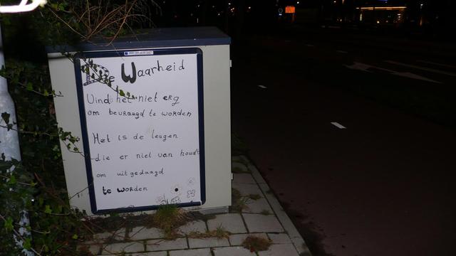 by night kastje op stoep naast fietspad. in de verte lichten. Wat begroieing 
witte poster met zwart beschreven, zie caption