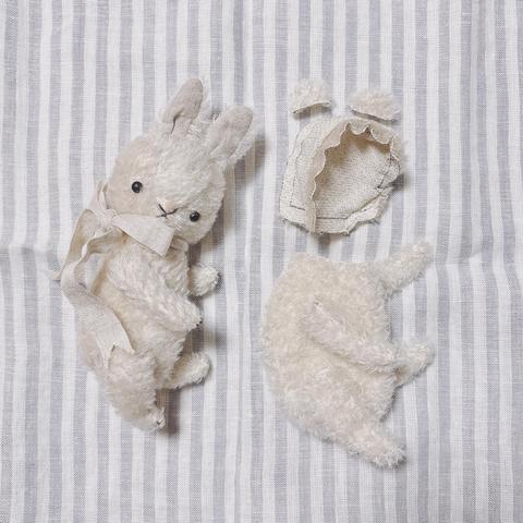 白いモヘア生地のテディベアのパーツを並べた様子(頭のみ仮縫い)、首にリボンを巻いた白いうさぎのぬいぐるみ