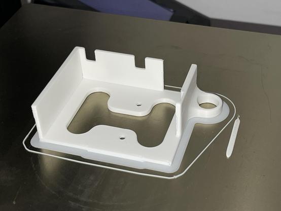 A square shaped box in the heat bed of a 3D printer. The object is printed with white filament and seems to be some sort of housing. Several parts in the walls are left out for buttons and latches.