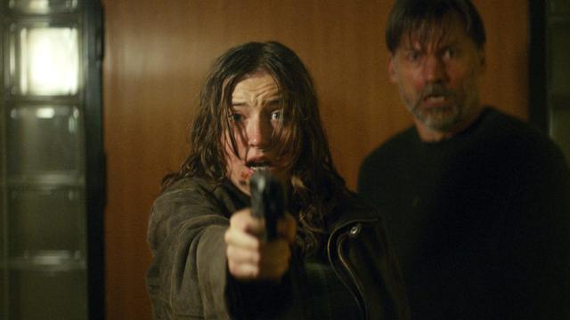 Emma (Fanny Leander Bornedal) hält eine Pistole in der Hand und zielt nach vorne. Sie hat leichte Verletzungen im Gesicht und sieht ängstlich aus. Hinter ihr steht Martin (Nikolaj Coster-Waldau), auch er sieht erschrocken nach vorn. (© ZDF/Lasse Frank Johannessen)