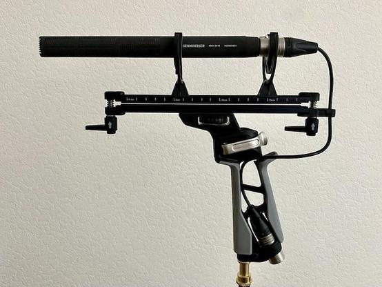 Photo of the side profile of a Sennheiser MKH-8018 microphone sitting in a windshield shock mount. A cable runs from the end of the mic to the bottom of the windshield pistol grip handle.