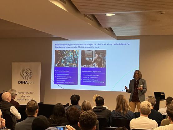 Person presents in front of a seated crowd at the conference. Slides with some GenAI pictures. Transcript:

Herausforderungen und Voraussetzungen für die Entwicklung und erfolgreiche Etablierung intermodaler Mobilitätsplattformen

- Technische Integration
- Standardisierte APis
-!Harmonisierte Buchungs-/
Vertriebsprozesse &
Businesslogik
• Verfügbarkeit von Echtzeitdaten
Kommerzielles & Organisation
Governance & Open Data
• Pflicht vs. Freiwilligkeit
• Geschäftsmodelle und
Profitabilität vs. Kostenverteitung