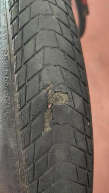 Pneu de vélo tellement usé qu'il n'y a plus de gomme et même un trou à travers la carcasse. On voit le sol orange à travers le trou