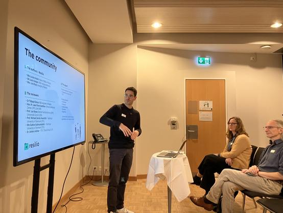 A presenter shows a slide titled „The community“ with a list of project partners.