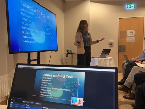 A person giving a talk raises hands in front of a screen of Issues with Big Tech