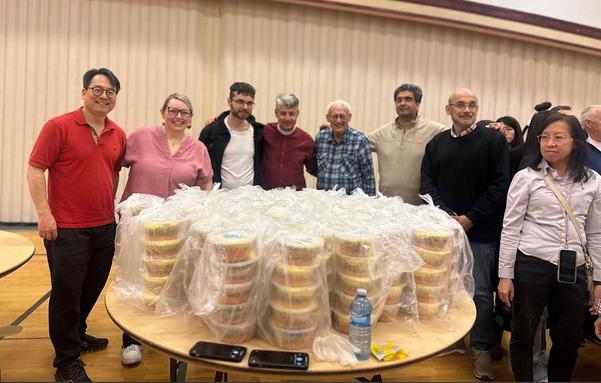 About a dozen people of different ages, genders, and ethnicities crowd around a table covered in ready-to-make soup bowls. Picture is from the Toronto Buddhist Temple Facebook page.