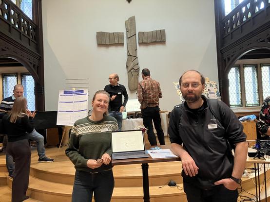 Participants of a conference showing their tech projects in front of a large cross