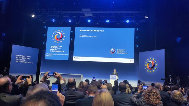 Eine breite Aufnahme eines Innenraums mit einer Bühne vor einer Menge von Personen. Auf der Bühne steht ein Podest und eine Person spricht vor einem Mikrofon. Im Hintergrund befindet sich ein großer Bildschirm mit einem Text auf blauem Hintergrund. Links und rechts vom Bildschirm stehen zwei Säulen.

Auf dem Bildschirm steht in weißer Schrift: "SUMMIT ON EUROPEAN SOVEREIGNTY entrepreneurs, investors, ladies and gentlemen." In der Mitte des Bildschirms befindet sich eine Grafik mit einem roten Kreis, der von einem weißen Stern umgeben ist, der von einem gelben Kreis umgeben ist, der von einem blauen Kreis umgeben ist. Über dem Text steht in kleinerer Schrift „Emmanuel Macron Präsident der französischen Republik.“ Die Menge besteht aus Personen, die sitzen und stehen, einige halten Mobiltelefone hoch. Die vorderen Reihen sind mit Personen gefüllt, und der Hintergrund ist dunkler und weniger detailliert.

Bereitgestellt von @altbot, privat und lokal generiert mit Gemma3:27b