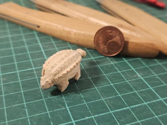 Foto eines aus Holz geschnitzten Ankylosaurus auf einer grünen Schneidematte. Im Hintergrund ein 5-Cent-Stück und einige Schneidewerkzeuge.