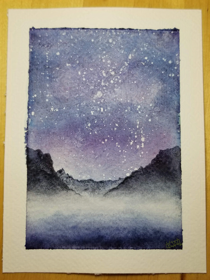 Watercolor landscape mountains silhouetted against a purple-blue sky full of stars. The base of the mountains are covered in mist, which stretches out onto the water below.