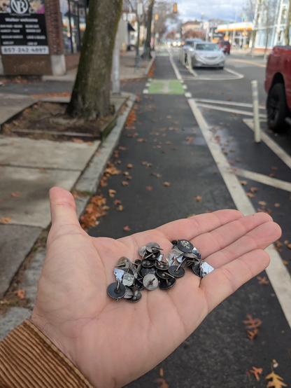 Photo of someone holding a handful of thumb tacks (~30) picked up from a bike lane in Cambridge, Massachusetts