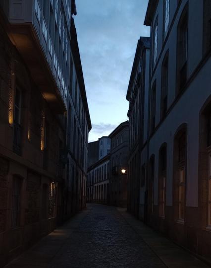 Narrow cobblestone street between tall historic buildings, dimly lit by streetlights, under an early evening blue and cloudy sky. Calm and serene ambiance.
#laureanoaraujo #santiagodecompostela #galiza
Santiago de Compostela, 18 de novembro de 2025