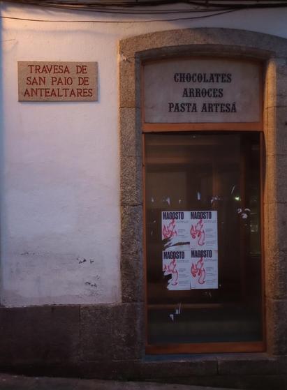 A cozy street scene shows a shopfront with a faded sign for chocolates, rice, and artisanal pasta. Magosto festival posters cover the window.
#laureanoaraujo #santiagodecompostela #galiza
Santiago de Compostela, 18 de novembro de 2025