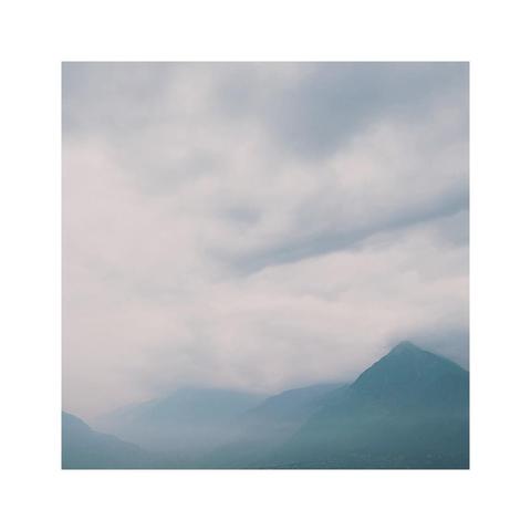 a subtle square image showing the details of a cloudy mountainscape. the sky is hazy after some rain but the early light is already coming through again. the layers of hills become more and more vague towards the distance