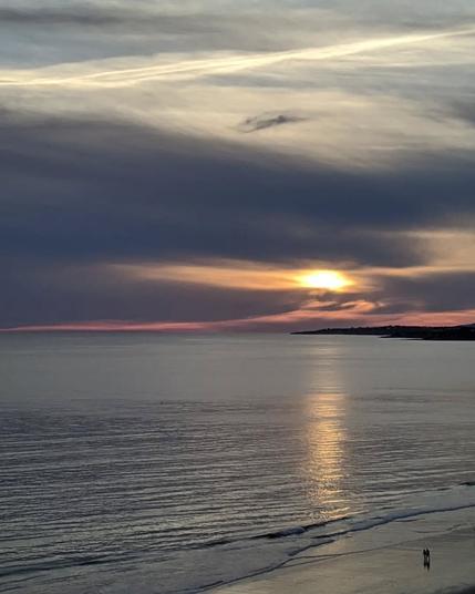 two persons walk by the sea looking at the sunset
