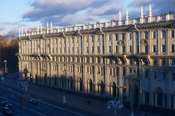 Th building on praspiekt Niezaliežnasci, 22, as viewed from the 4th floor window of GUM (Main Department Store), in the daytime. Sky is a bit cloudy but blue, a few pedestrians are seen, as well as three cars on praspiekt Niezaležnasci.