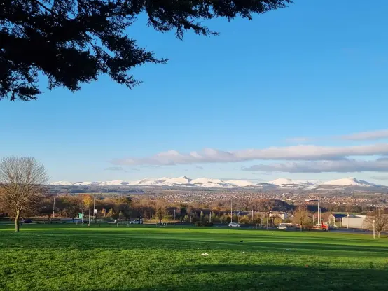 Panorama picture of Pentland Hills covered in snow with the Newbattle High School's park in the foreground still green