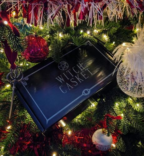 Black shoebox size box with the Witch Casket logo on top, in the midst of the white fairy lights and decorations and green branches of my Christmas tree