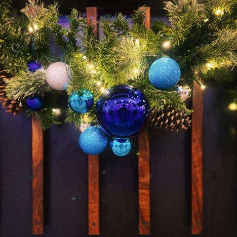 Christmas wreathes, blue and white baubles, and pinecones drape against a purple and brown wooden coffee shop counter, the largest central bauble reflecting me snapping a photograph.