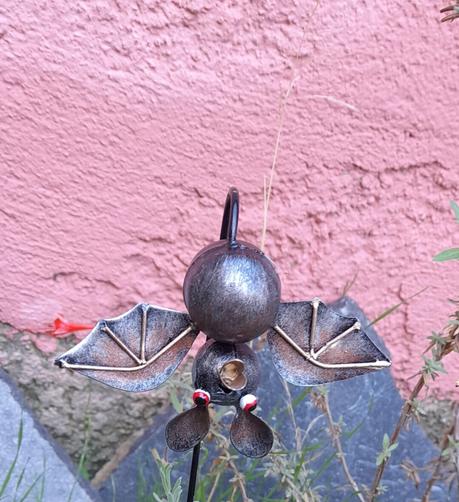 Petite chauve-souris en métal, ailes ouvertes et tête en bas.