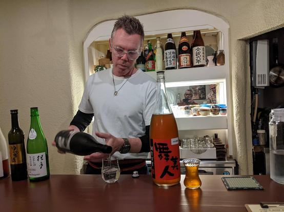 Bartender pouring sake into a glass in a small bar