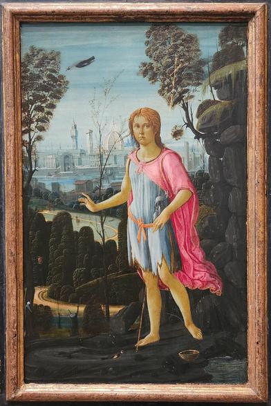 An adolescent John the Baptist in foreground wearing his distinctive animal skins and gesturing with his right hand. In the background are hills, fields and a city with large dome in the distance.
