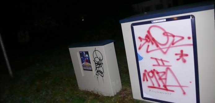 twee kastjes by night. het achterste kleinere kastje heeft een gewone poster en graffiti tag
het voorste kastje een reclame frame met witte poster en rode graffiti tekst, als in caption