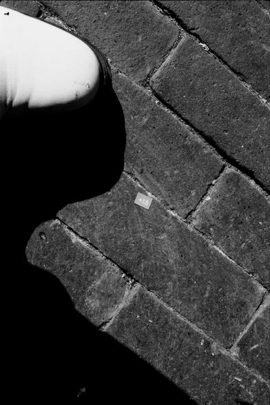 Tiny piece of paper on a stone floor, saying +1,5. A white shoe in the upper left corner, a sharp wobbly shadow on the left.