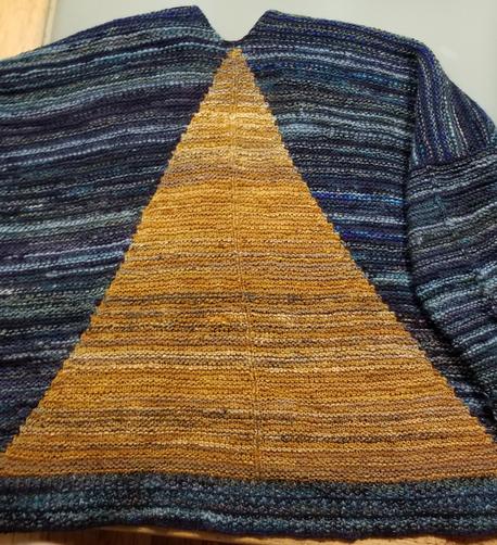 The back of an oversize knit cardigan, with a large yellow triangle on a blue field, laid out flat on a table.