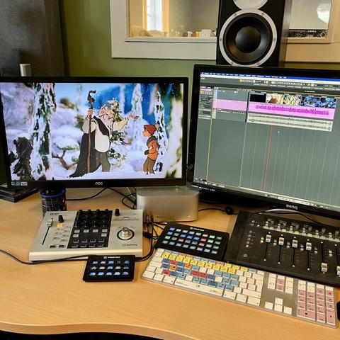 POV-bilde fra komponist arbeidende i et lydstudio med to skjermer. På høyre skjerm sees lydbølger i en DAW-programvare (Nuendo), mens på venstre skjerm et stillbilde fra en animasjonsfilm. Bildet er av en snødekket skog der en trollmann snakker med en liten gutt.