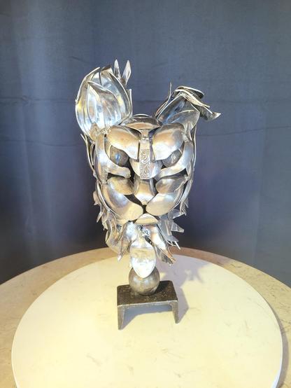 Une tête de chat grognon fait entièrement de cuillères. 
Elle fait environ 1'de haut. Une de ses oreilles est pliée.