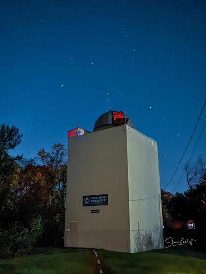 The Westport Observatory tower illuminated under a clear starry night sky with visible Orion constellation.