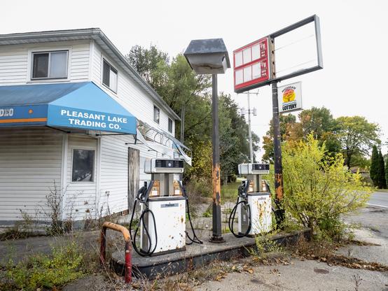 An abandoned gas station with a visible Michigan Lottery sign hanging off the empty prices sign.
