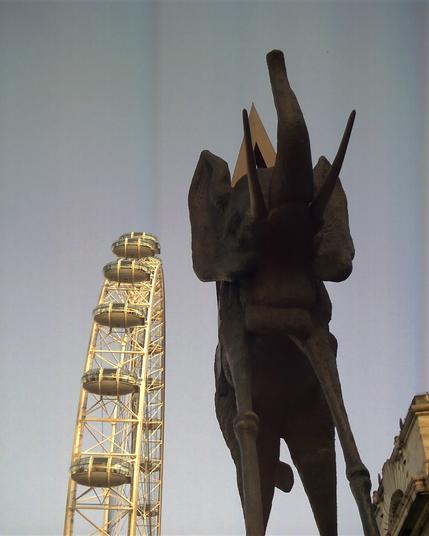 Looking up a the edge of a Ferris wheel with futuristic capsules on the right and a surreal sculpture of an elephant with elongated legs on the left.
