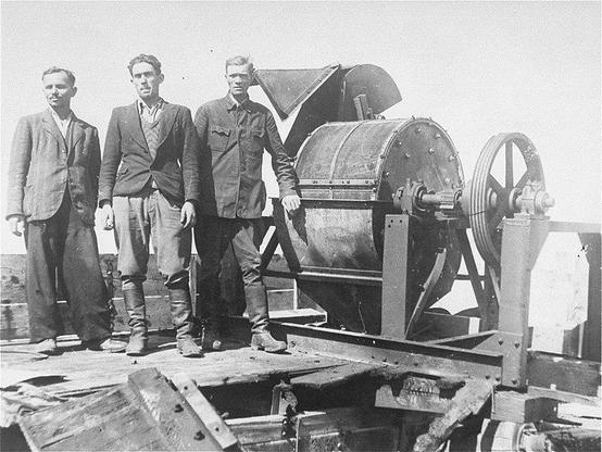 Survivors of a Sonderkommando 1005 unit stand next to a mill used to crush bones at the Janowska concentration camp following its liberation in 1944. By Jewish prisoners forced to work for a Sonderkommando 1005 unit pose next to a bone crushing machine in the Janowska concentration camp ushmm.org [1], Public Domain, https://commons.wikimedia.org/w/index.php?curid=76080171